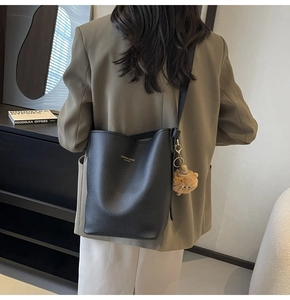 Close-up of black lychee leather bucket bag with golden lettering and a cute bear charm