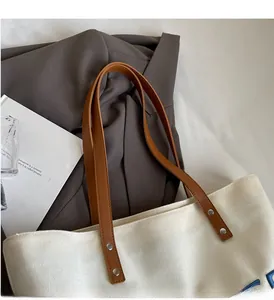 Détail du cabas en toile montrant les poignées en cuir marron et rivets argentés
