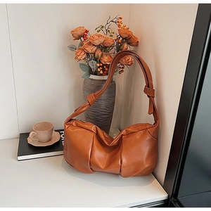 Close-up of caramel brown ruched leather shoulder bag with decorative knotted strap detail