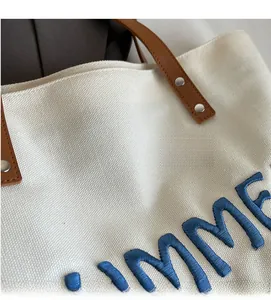 Détail de la toile écrue avec broderie bleue et poignée en cuir marron sur le cabas