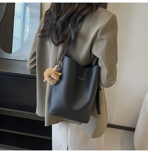 Close-up of black lychee grain bucket bag with golden text and a brown lion plush charm