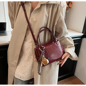 Détail du sac bandoulière en similicuir bordeaux avec breloque baseball sur trench-coat