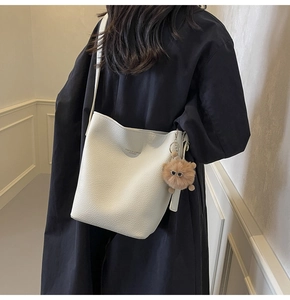 White bucket bag with litchi grain texture and a cute brown pompom charm shown on model