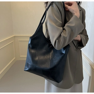 Detail of black leather tote bag with geometric patchwork and slim dual shoulder straps