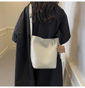 Detail of white lychee leather bucket bag with brown plush pendant worn by a model