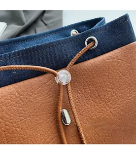 Detail of blue denim and brown leather backpack featuring a drawstring and metal eyelets