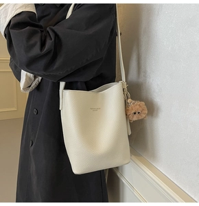 Detail of cream bucket bag with litchi grain texture and brown plush dog charm