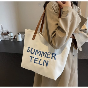 Détail du sac cabas en toile blanche avec broderie bleue et bandoulière en cuir