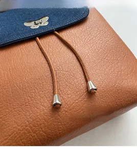 Detail of blue denim flap and brown leather backpack with silver butterfly buckle