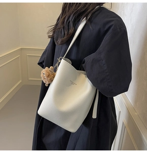 Close-up of white pebble leather bucket bag with text print and brown plush charm