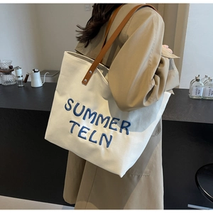 Détail du sac cabas en toile blanche avec broderie bleue et bandoulière en cuir marron