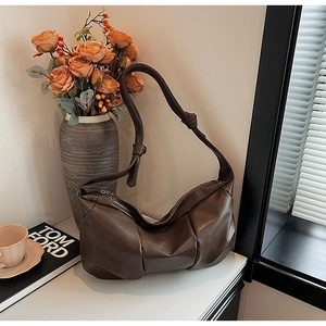 Detailed view of dark brown pleated leather handbag with knot strap on a scenic background