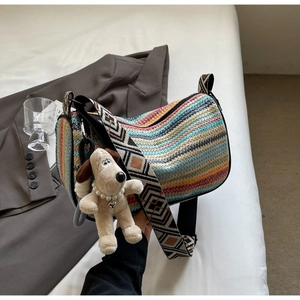Detail of colorful knitted cylinder bag with a plush charm on a white bed sheet