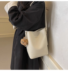 Close-up of white pebble leather bucket bag with fashion text and plush doll accessory