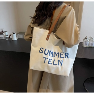 Détail du grand sac cabas en toile avec broderie bleue et poignées en cuir marron élégantes