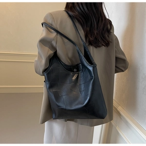 Detail of black geometric patchwork tote bag shown on model with magnetic buckle