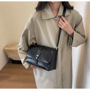 Detail view of the black leather crossbody bag featuring a golden buckle on the flap