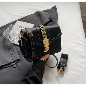 Detail of black crossbody bag featuring white stitching and chunky gold chain strap