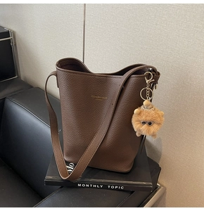 Detail of dark brown pebble leather bucket bag with a cute plush charm on a book