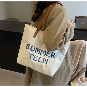 Détail du cabas en toile blanc cassé avec broderie bleue et lanière en cuir marron