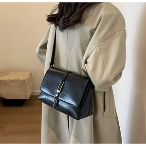 Close-up of black retro leather flap bag with gold hardware worn over beige trench coat