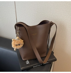 Brown litchi grain leather bucket bag featuring a wide strap and cute plush bear charm