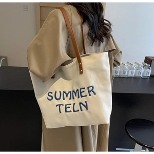 Détail du sac cabas en toile blanc cassé avec broderie bleue et anses en cuir marron