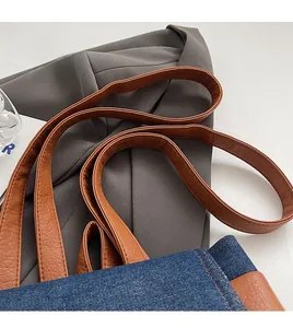 Detail of blue denim backpack with brown leather strap and reinforced stitching
