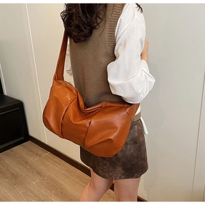 Caramel brown soft leather crossbody bag with pleated cloud design shown on model's shoulder