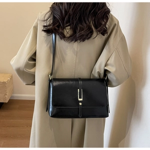Detailed back view of a chic black flap bag with gold hardware worn over a beige coat