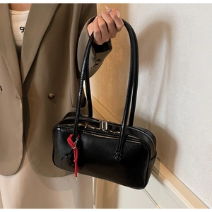 Gros plan d'un sac bowling en cuir verni noir avec un gland tressé rouge vif décoratif