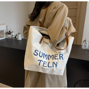 Détail du sac cabas en toile avec broderie bleue et poignées en cuir marron élégant