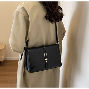 Detail of a black leather crossbody bag with a gold buckle worn with a beige trench coat