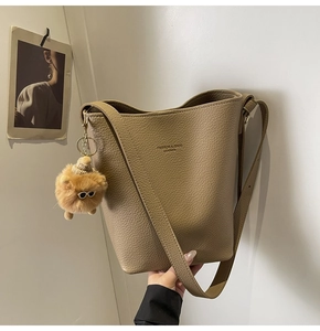 Detail of tan lychee grain leather bucket bag featuring a cute plush ball keychain