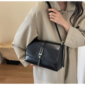 Detail of black pleated leather bag with gold bar metal buckle on beige trench coat