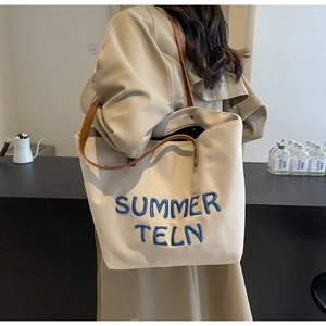Détail du sac cabas en toile blanc cassé avec broderie bleue et poignées en cuir marron