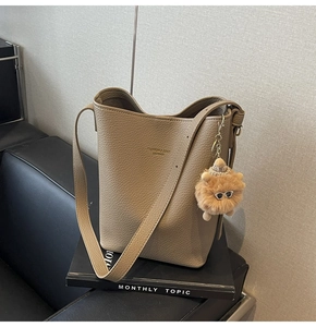 Detail of taupe litchi grain leather bucket bag with plush bear charm and long strap