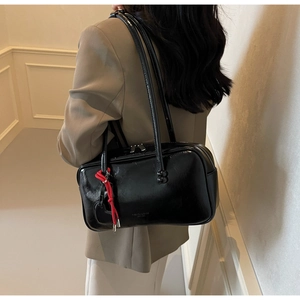 Détail d'un sac à bandoulière noir brillant avec breloque en corde rouge et imprimé tendance