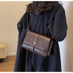 Detail of dark brown vintage leather crossbody bag worn over a stylish black coat