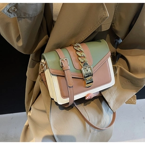 Detail of color-block flap bag with gold chain handle and vintage buckle on trench coat
