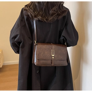 Detail of vintage brown leather crossbody bag with elegant gold buckle on black coat