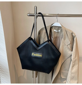 Detailed view of black pleated tote bag with V-shaped cut and yellow fashion patch
