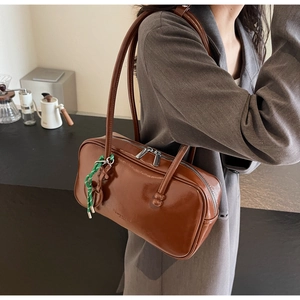 Détail du sac bowling vintage en cuir marron brillant avec pendentif vert tressé