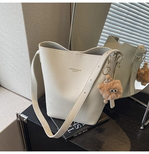 Detailed view of white pebble leather bucket bag with plush bear charm and long strap