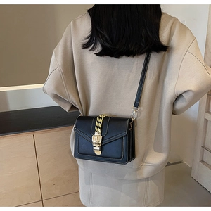 Detail of black leather crossbody bag with gold chain ornament and metal clasp buckle