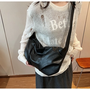 Detail of a black pleated cloud bag with soft leather texture and long shoulder strap