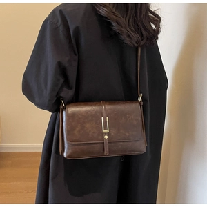 Brown vintage rectangular crossbody bag with golden metal buckle on black coat