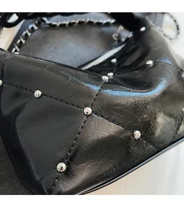 Detail of black glossy pleated leather bag with silver studs and metal chain strap