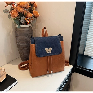 Detail of denim and brown leather patchwork backpack with gold butterfly buckle and tassels