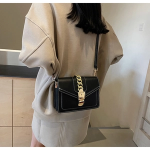 Detail of black crossbody bag with white stitching and decorative gold chain strap